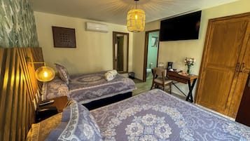 A hotel room with two beds, a desk, a chair, a TV mounted on the wall, and a wooden wardrobe.