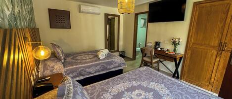 A hotel room with two beds, a desk, a chair, a TV mounted on the wall, and a wooden wardrobe.