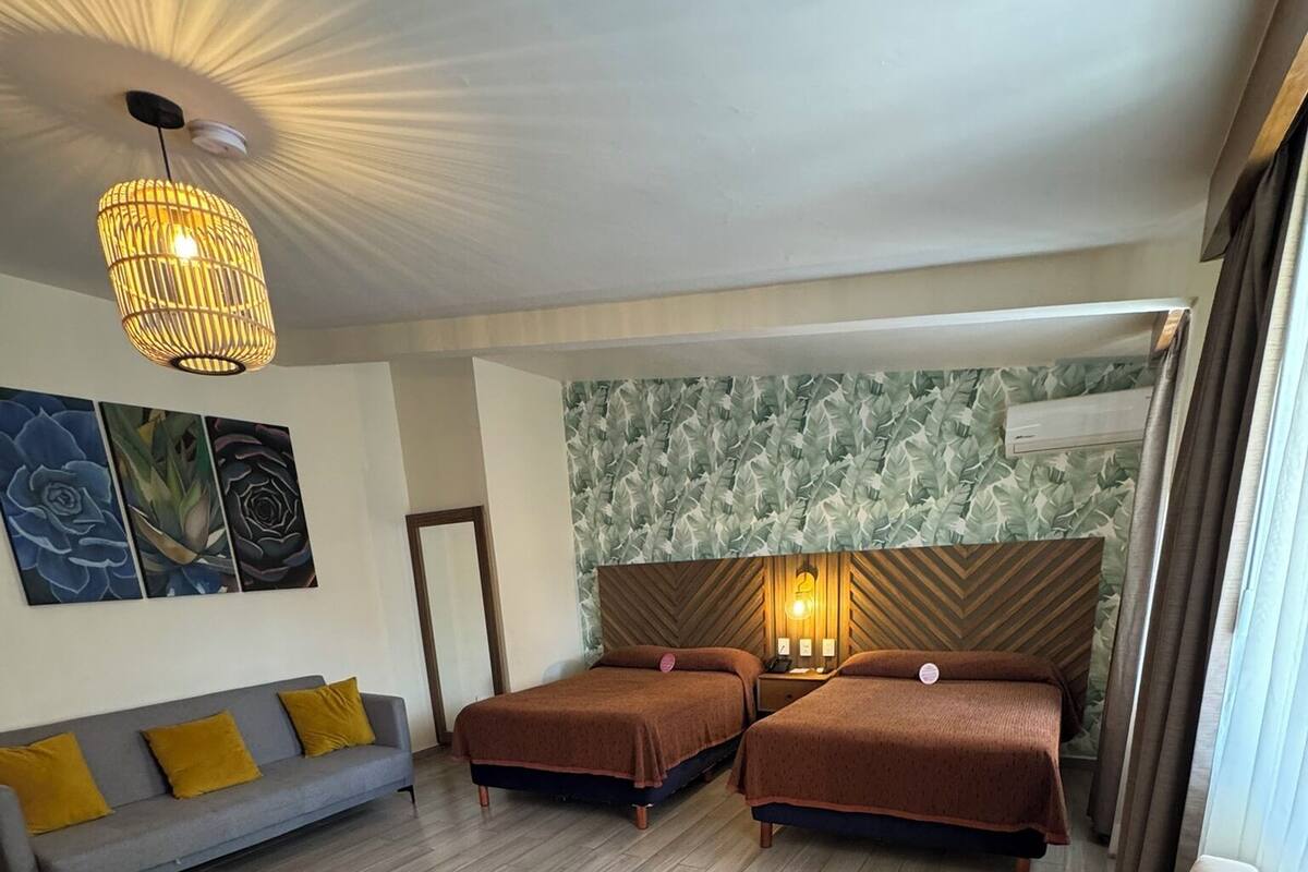Habitación de hotel con dos camas individuales, un sofá, una silla y una lámpara decorativa en el techo.