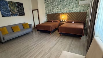 A hotel room with two single beds, a sofa, a chair, and a decorative ceiling light.