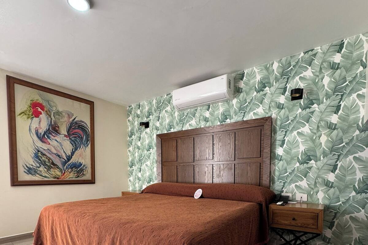 Un dormitorio con una cama de madera, una mesita de noche, aire acondicionado de pared y una lámpara en el techo.