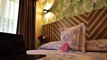 A hotel room with a bed, a laptop on the bed, a wall-mounted light, and a decorative leaf-patterned wall.