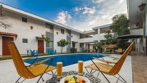 A poolside area with two wicker chairs, a table with fruit and drinks, and a swimming pool. - Hotel Isabel (Guadalajara)
