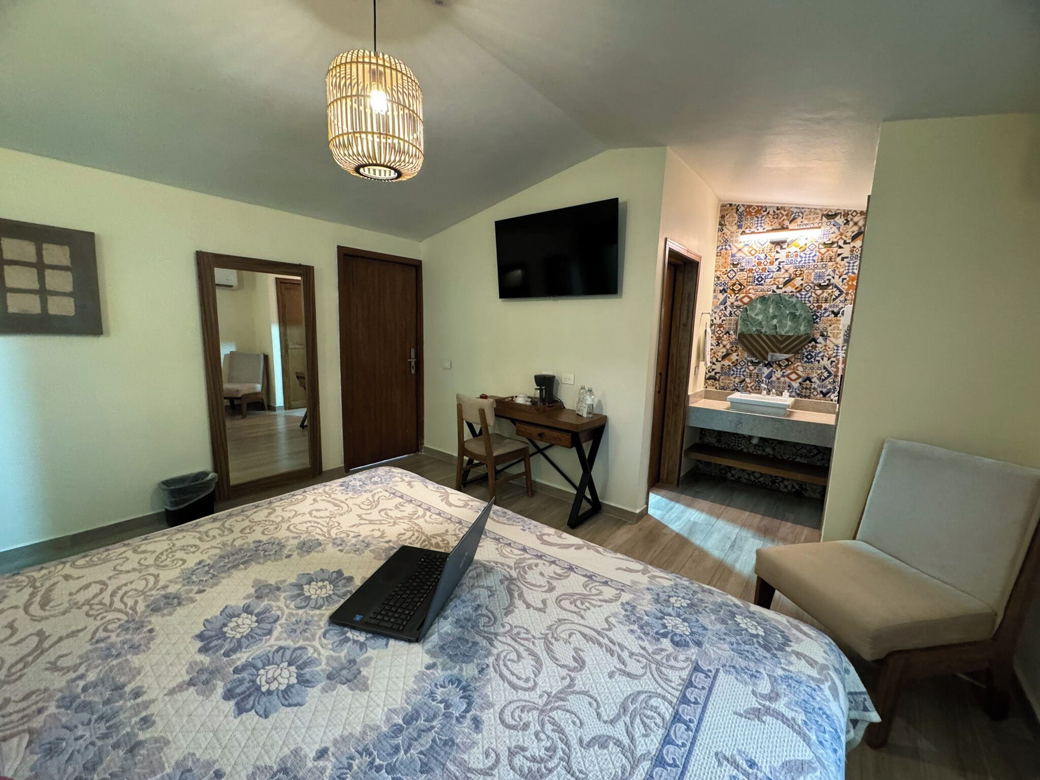 A bedroom with a bed, a desk, a chair, a television, and a bathroom with a tiled backsplash.