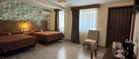 A hotel room with two beds, a desk with a coffee maker, a chair, and a large window with curtains.