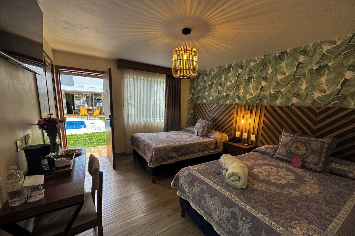 Habitación de hotel con dos camas, un escritorio y una silla. Se ve una piscina fuera.