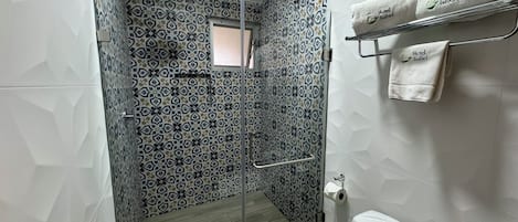 Un baño con azulejos estampados, cabina de ducha con paredes de vidrio, inodoro y un perchero con toallas.