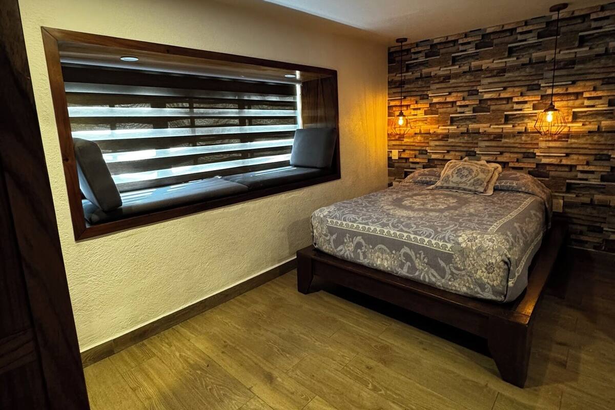 Un dormitorio con cama, ventana con persianas, suelo de madera y pared de piedra.