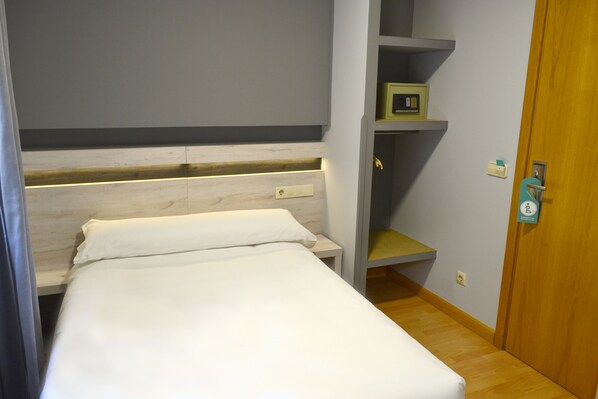 Una cama individual con cabecera de madera, una mesita de noche y una estantería con un objeto pequeño encima.