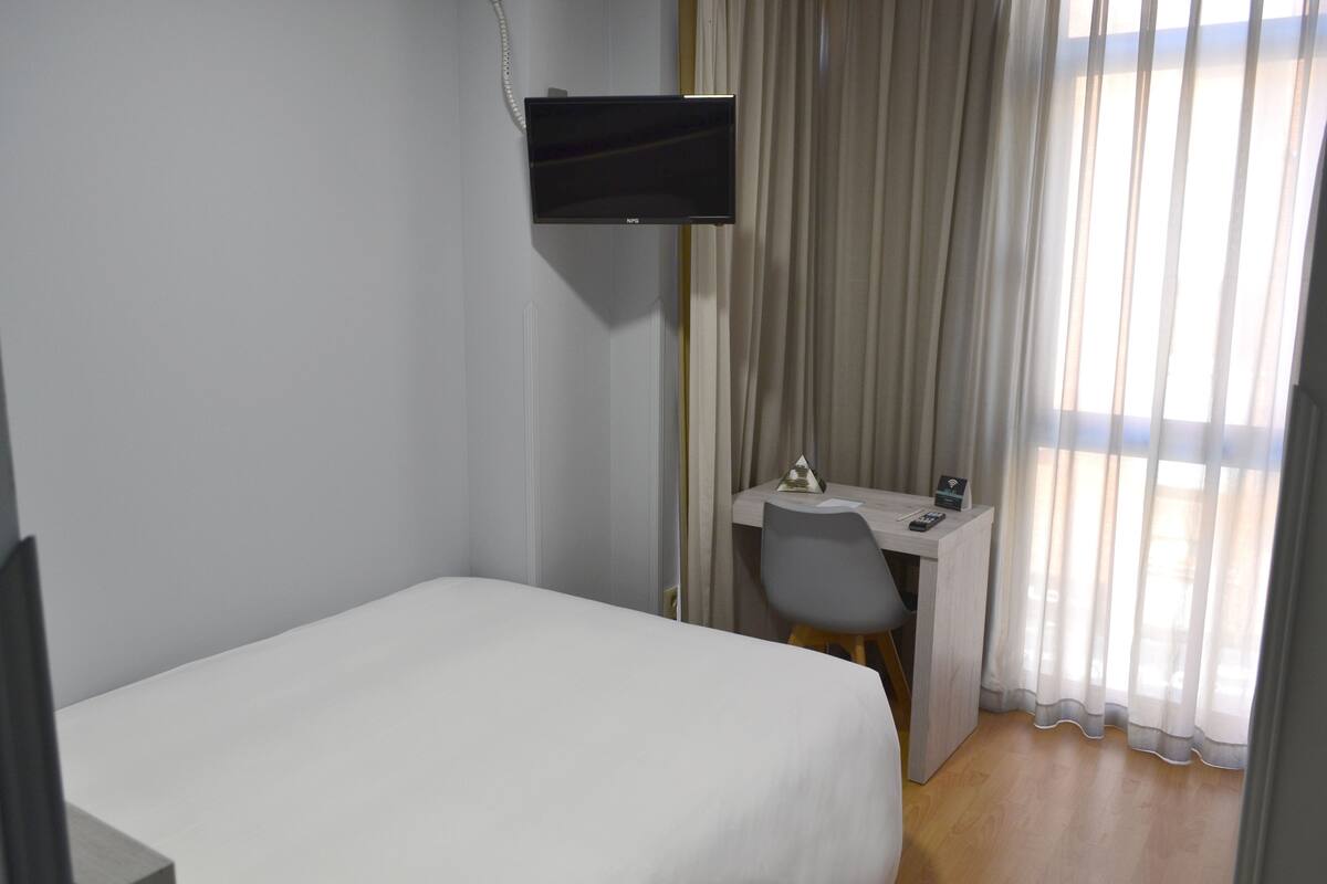 Hotellihuone, jossa on sänky, työpöytä, tuoli ja seinälle asennettu televisio.