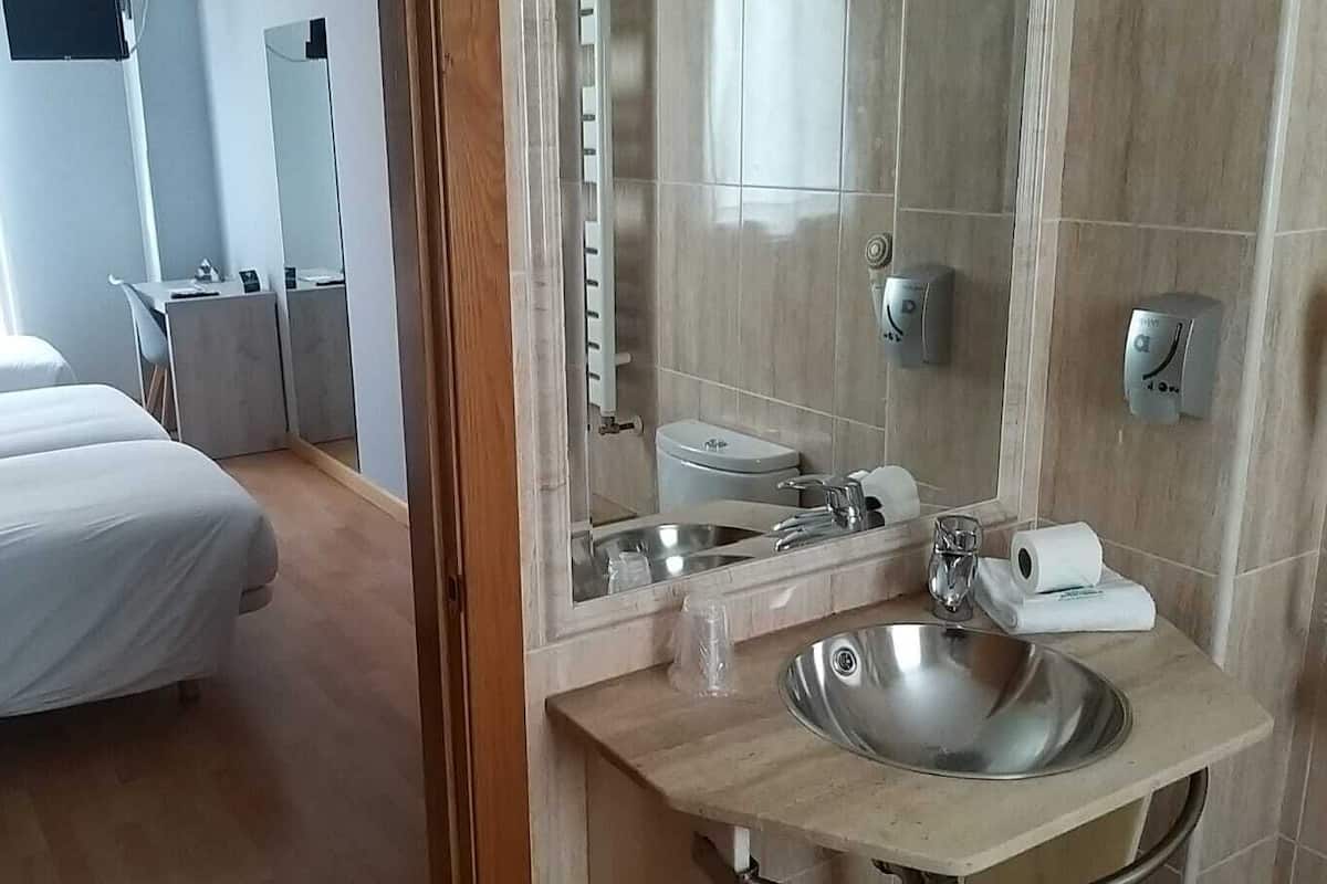 Hotellihuone, jossa on sänky, kylpyhuone, jossa on pesuallas, peili ja wc.