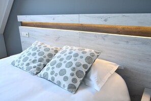 Una cama con ropa de cama blanca y dos almohadas con un estampado circular gris y blanco.