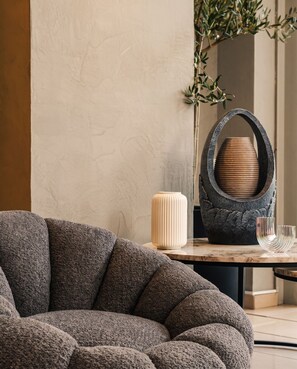 Un salón moderno con un sofá texturizado, una mesa de mármol y elementos decorativos, incluyendo un jarrón y una escultura metálica única.