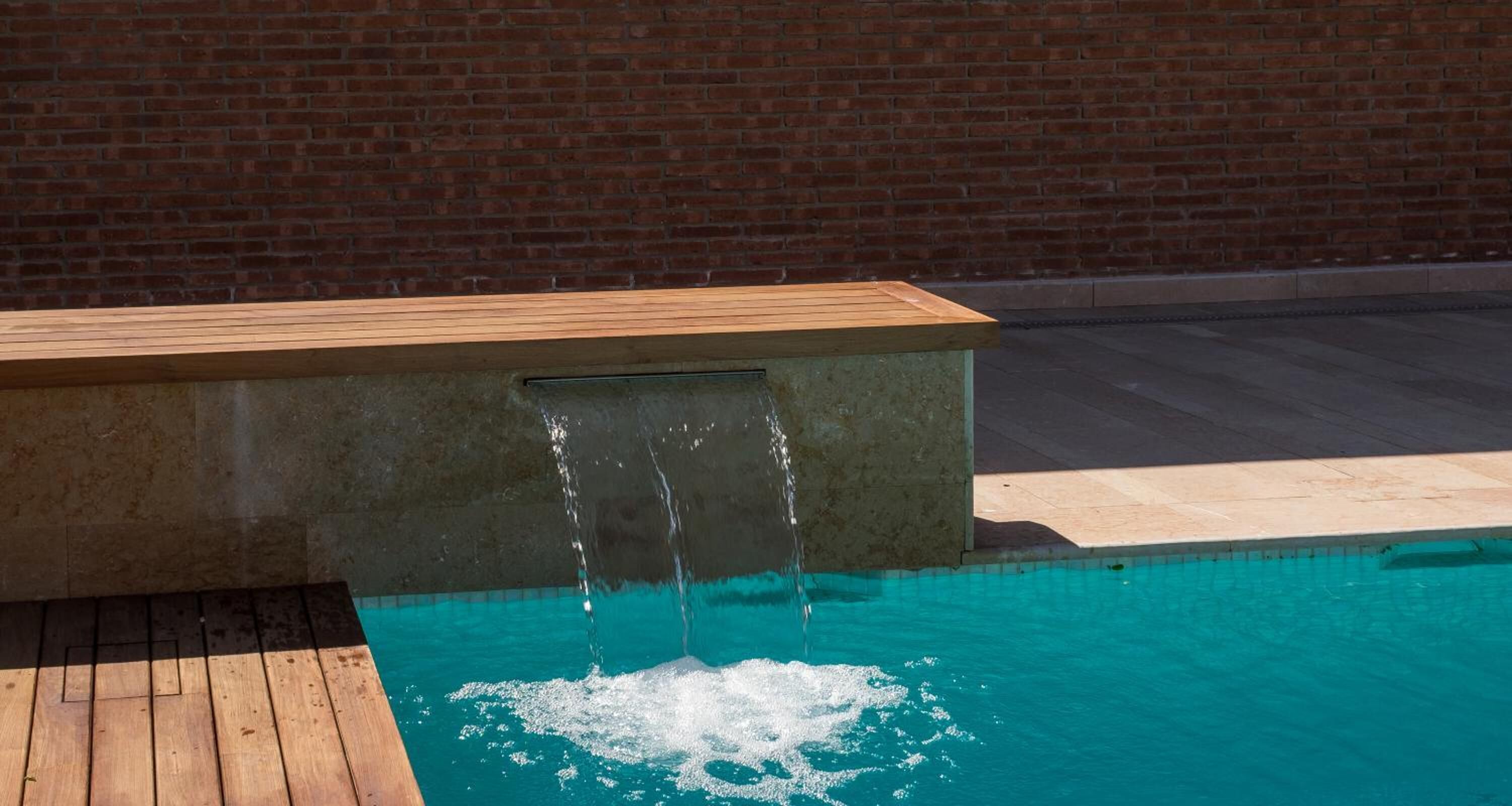 Una piscina con un pontile di legno e un muro di mattoni sullo sfondo.