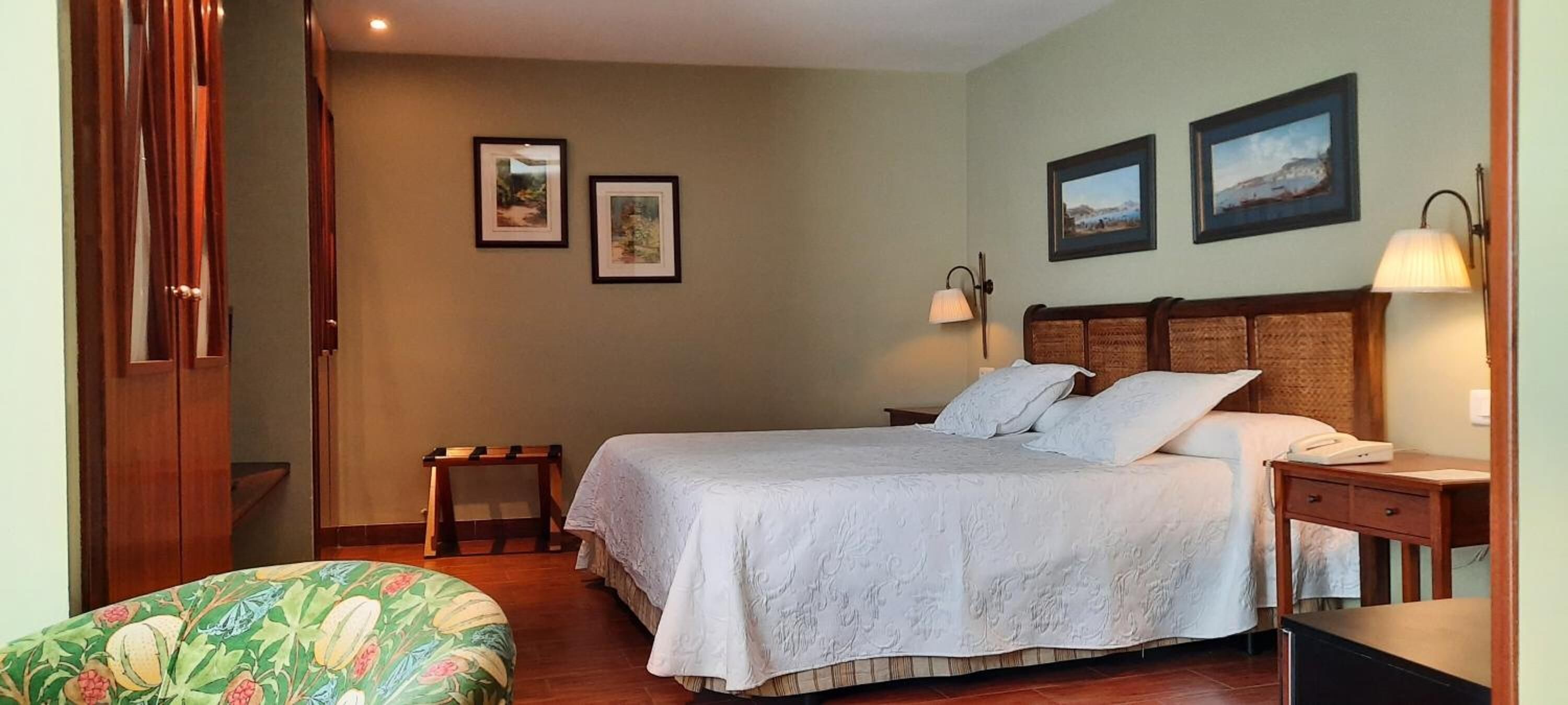 A bedroom with a bed, bedside tables, a nightstand, a chair, and framed pictures on the wall.