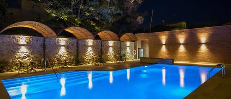 A swimming pool with a clear blue water surface, surrounded by stone walls and arched structures.