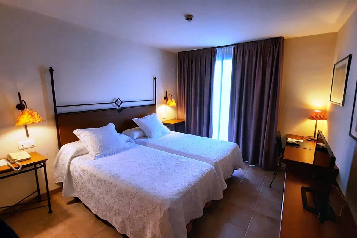 A hotel room with two beds, a desk with a chair, a telephone, and two lamps.