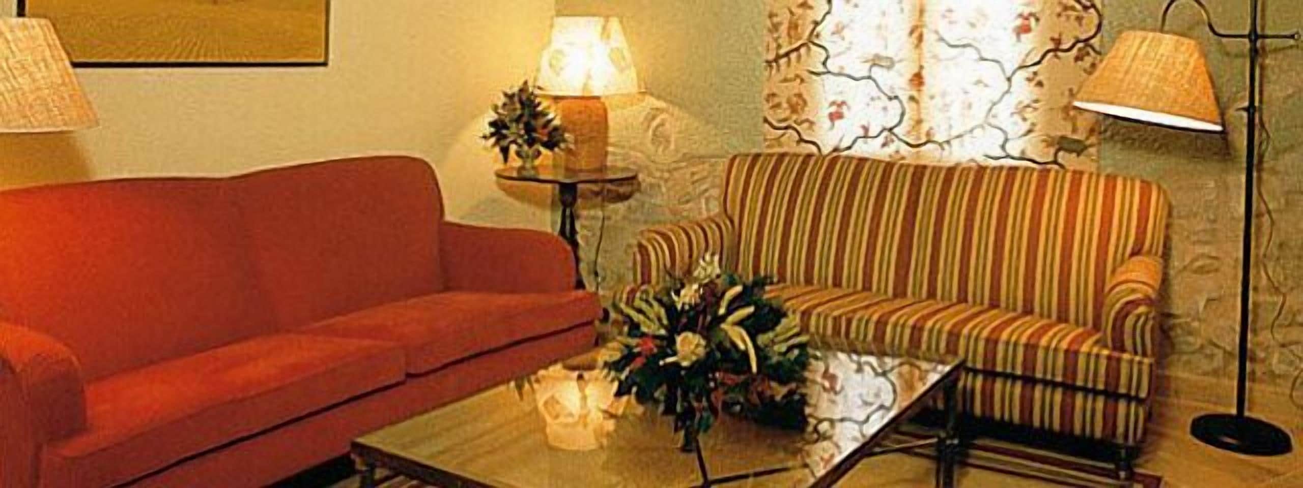 Una sala de estar con un sofá rojo, un sofá a rayas, una mesa de centro y dos lámparas de pie.
