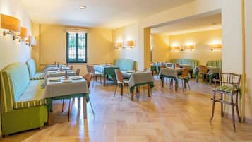 A dining area with green-striped sofas and tables, wooden flooring, and wall-mounted lamps.