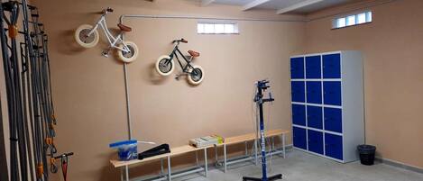A room with two bicycles mounted on the wall, a bench, a table with items, and a blue locker.