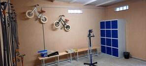 Een kamer met twee fietsen aan de muur, een bank, een tafel met spullen en een blauwe kast.