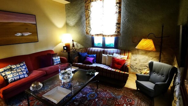 Un salon chaleureux avec un canapé rouge, un canapé à rayures et un fauteuil gris. On y trouve une table basse en verre, une lampe et un tableau accroché au mur.