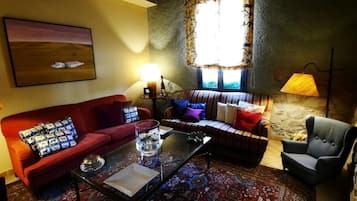 A cozy living room with a red sofa, striped sofa, and a grey armchair. There is a glass coffee table, a lamp, and a painting on the wall.