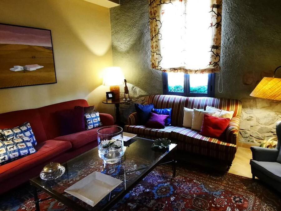 A cozy living room with a red sofa, striped sofa, and a grey armchair. There is a glass coffee table, a lamp, and a painting on the wall.