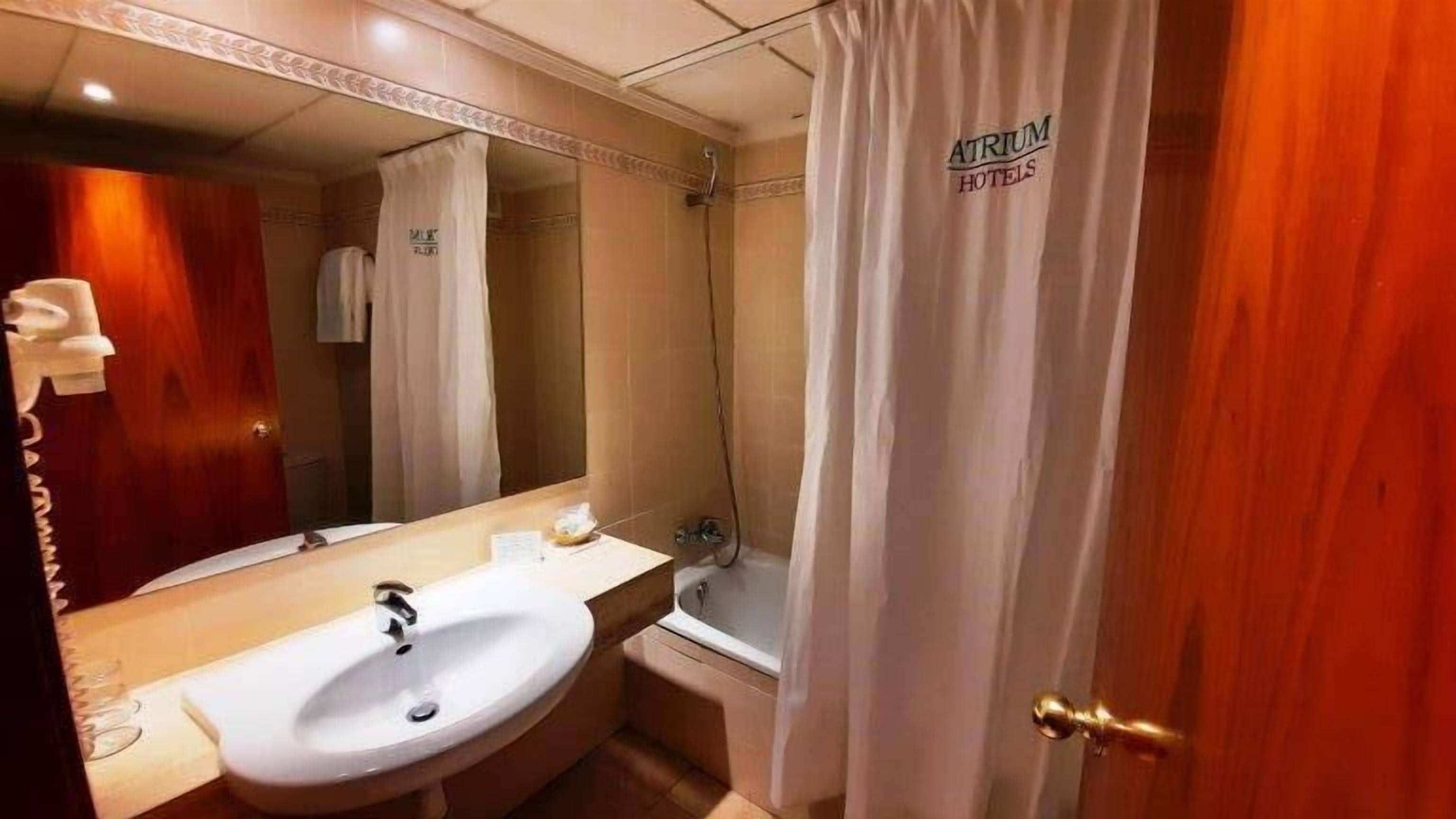 A bathroom with a sink, mirror, shower, and a door with a curtain.