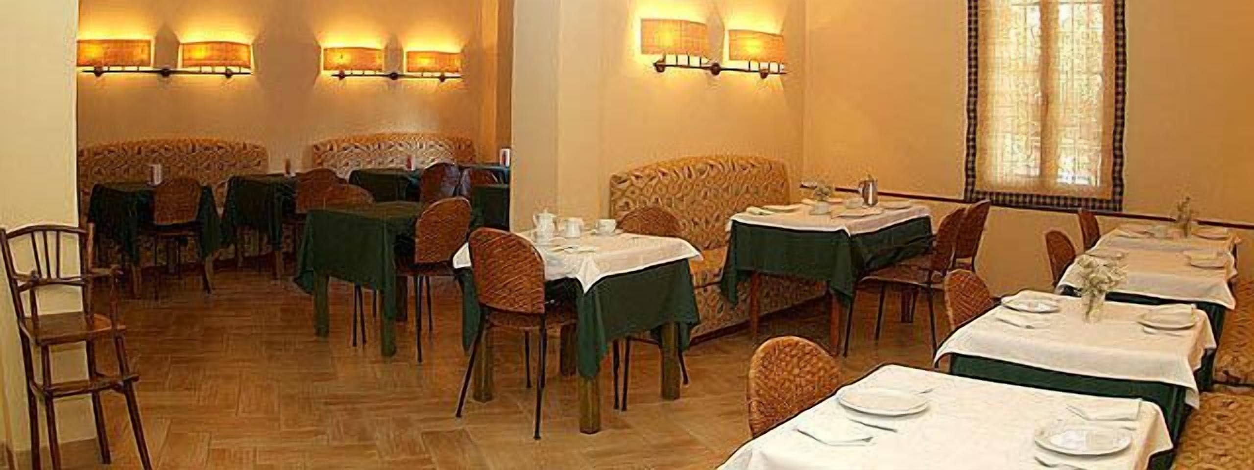 A restaurant with multiple tables and chairs, some with green tablecloths.