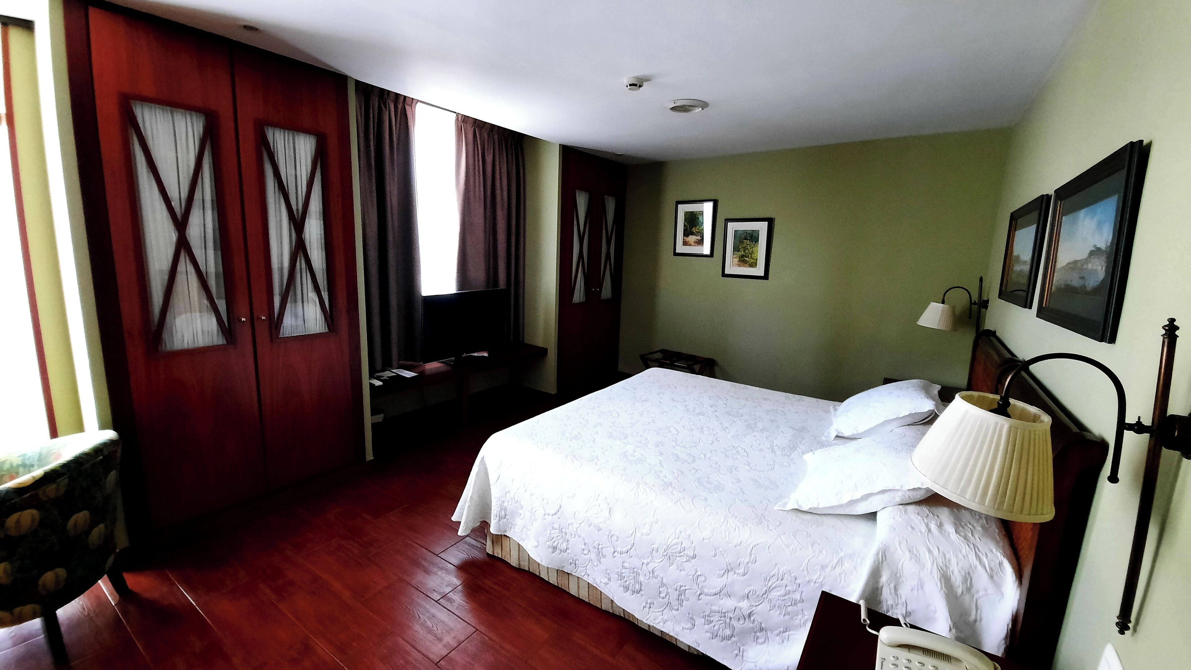 Habitación de hotel con una cama grande, un escritorio con silla, un televisor y dos cuadros en la pared.