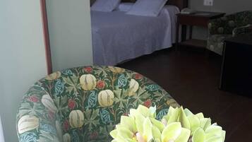 Una habitació amb un llit, una cadira i una taula amb un ram de flors.