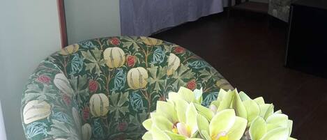 A room with a bed, a chair, and a table with a vase of flowers.