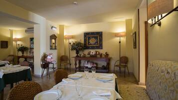 A dining area with a table set for four, chairs, a sofa, and wall-mounted lamps.