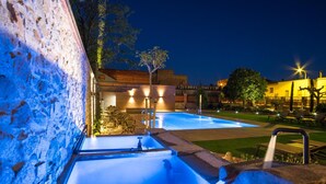 Un espace extérieur avec piscine, aménagé pour la baignade nocturne, comprenant un mur en pierre, une fontaine et des chaises longues.