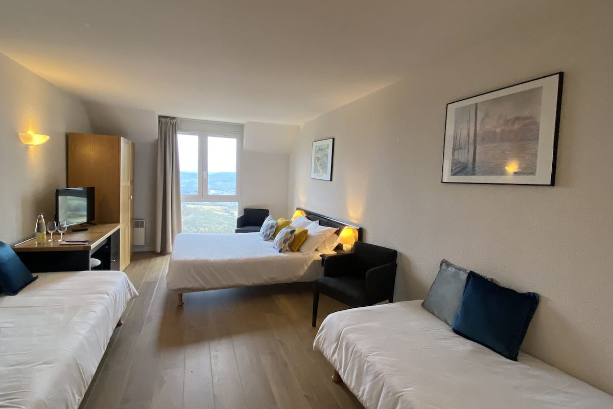 A hotel room with two beds, a desk with a computer, a chair, and a large window offering a view of the outdoors.