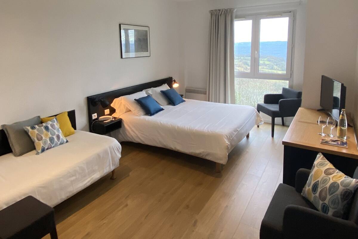 A hotel room with two single beds, a desk with a chair, a TV, and a window with a view.