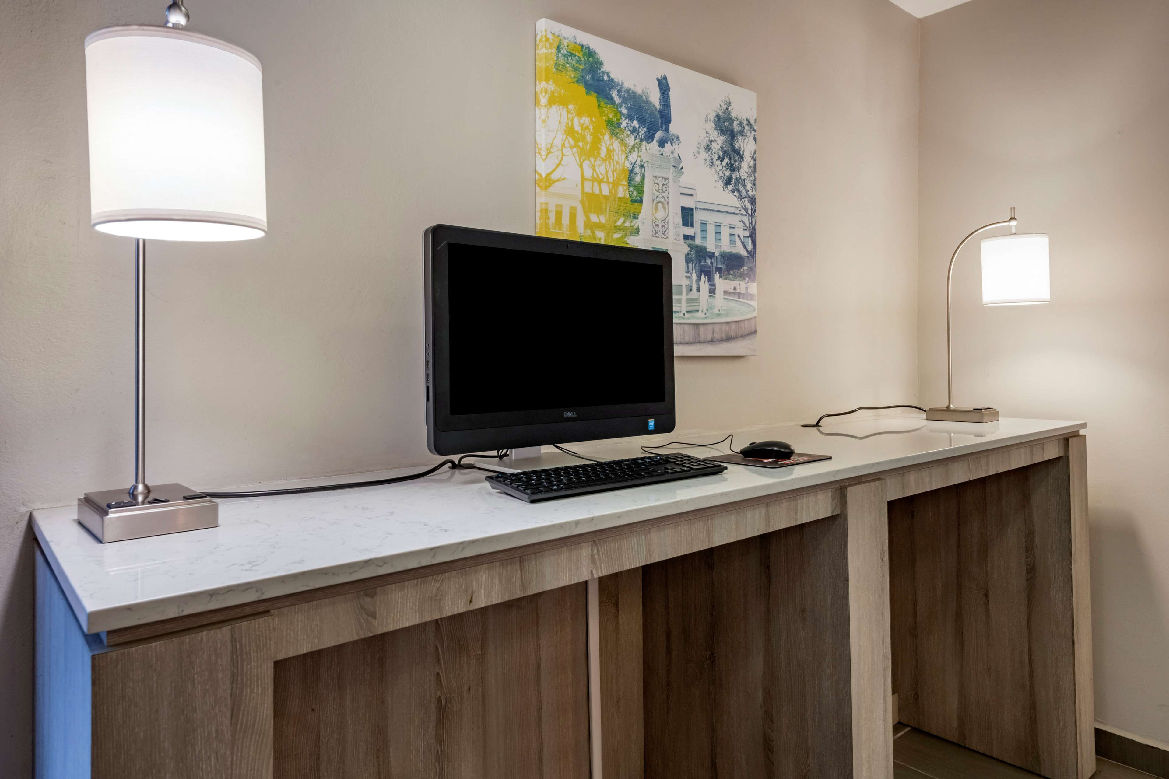 A hotel reception desk with a computer, keyboard, and mouse, flanked by two lamps.