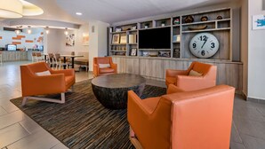 A modern lobby with orange seating, a round coffee table, and a wall-mounted clock.