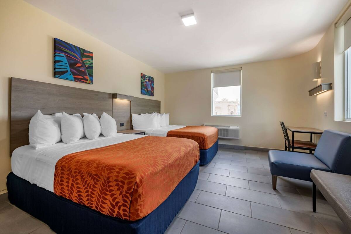 Ein Hotelzimmer mit zwei Betten, einem Schlafsofa, einem Tisch und Bildern an den Wänden.