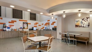 A modern restaurant with a central counter, seating area, and a mural on the wall.
