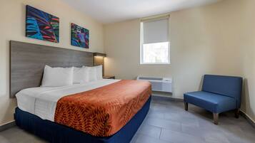 A hotel room with a bed, a blue armchair, and two abstract paintings on the wall.