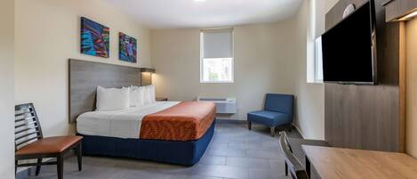 Una habitación de hotel con cama, escritorio, silla, televisor y obras de arte en la pared.