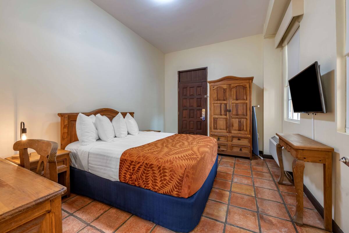 Ein Schlafzimmer mit einem Bett, Holzmöbeln, einem Fernseher und einem Fliesenboden.