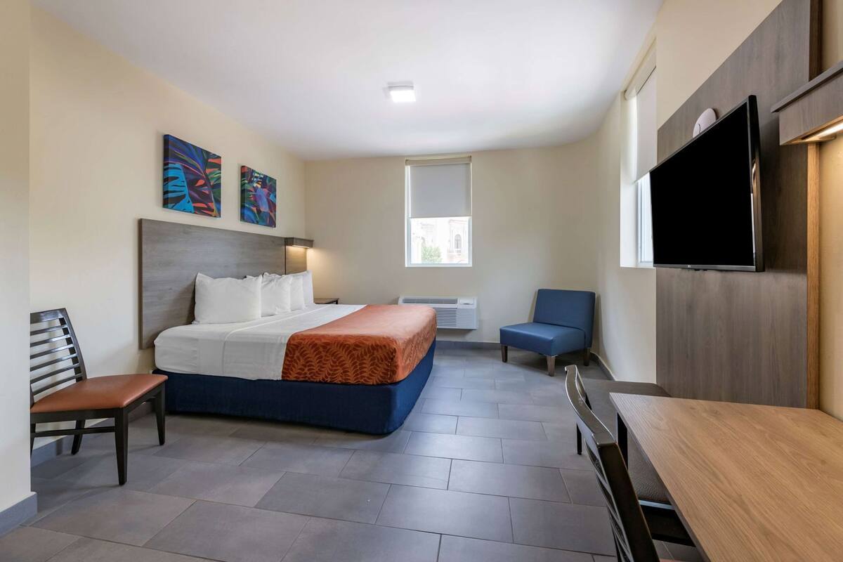 Ein Hotelzimmer mit Bett, Schreibtisch, Sessel, Fernseher und Bildern an der Wand.