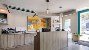 A hotel reception area with a wooden reception desk, air conditioning unit, and a large abstract painting on the wall.