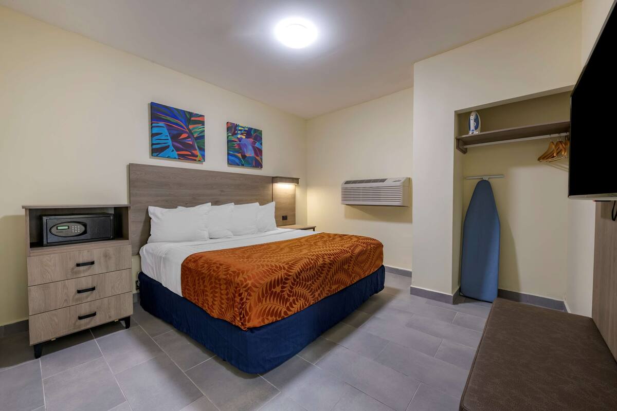 Ein Hotelzimmer mit einem Bett, einem Nachttisch mit Radio, einer Wand-Klimaanlage und einem Regal mit Kleidung und einem Fernseher.