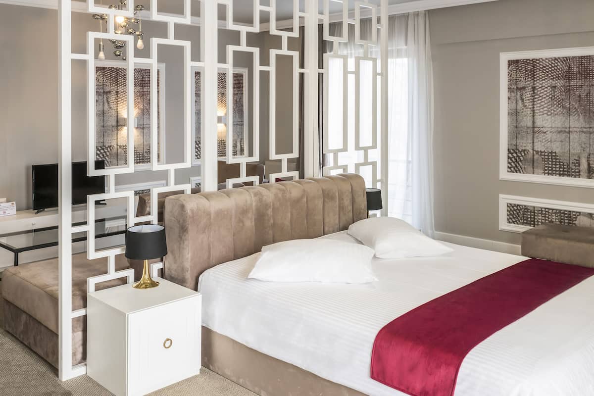 A modern hotel room with a large bed, a white nightstand, a TV, and a decorative white partition.