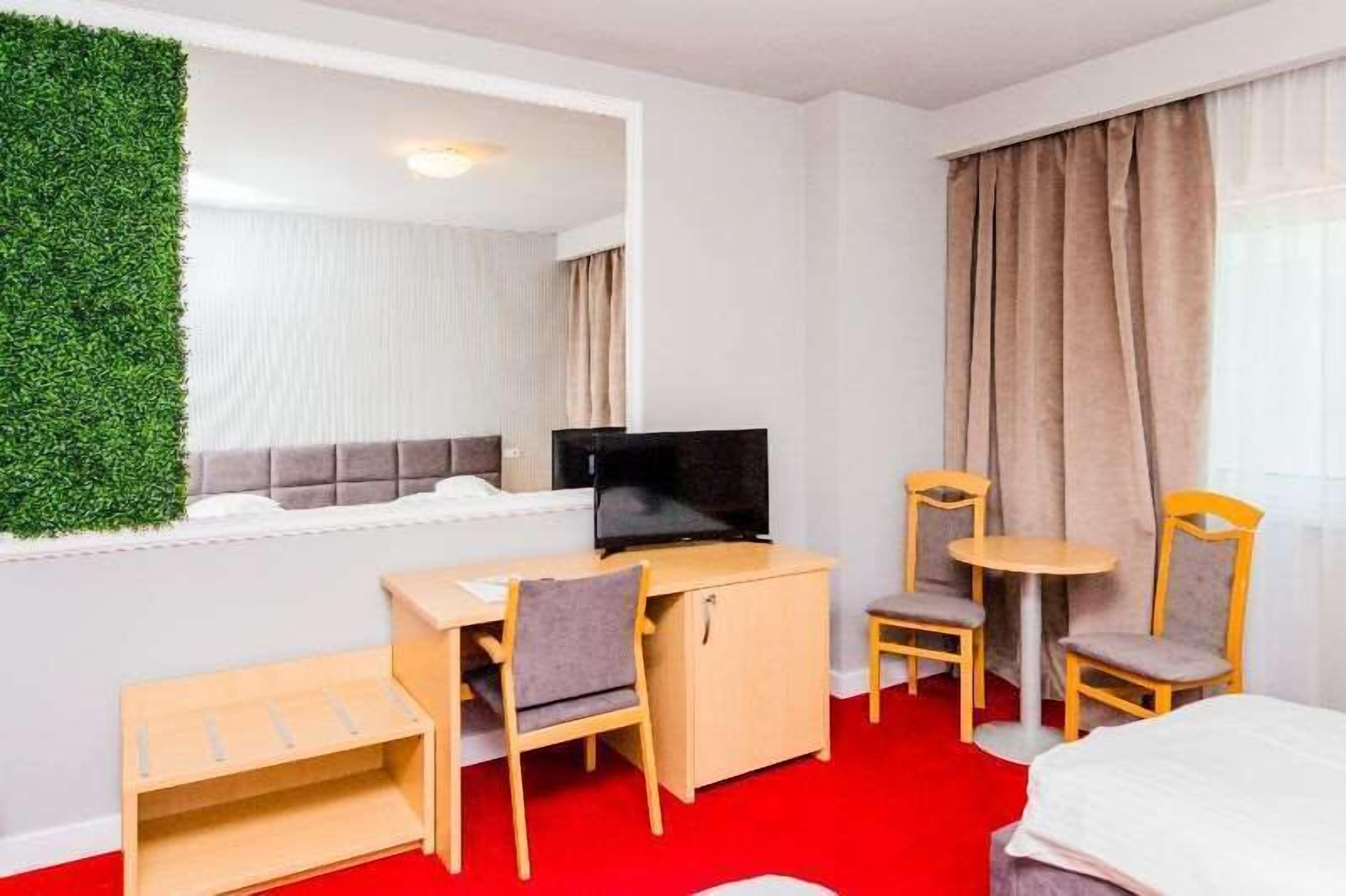A hotel room with a bed, a desk with a chair, a television, and a small table with two chairs.