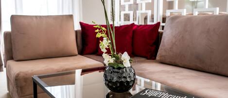 Uma sala de estar moderna com uma mesa de centro de vidro, um sofá com almofadas vermelhas e um vaso com flores.